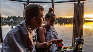 Un couple est assis à une table, devant un lac, et admire le coucher de soleil.