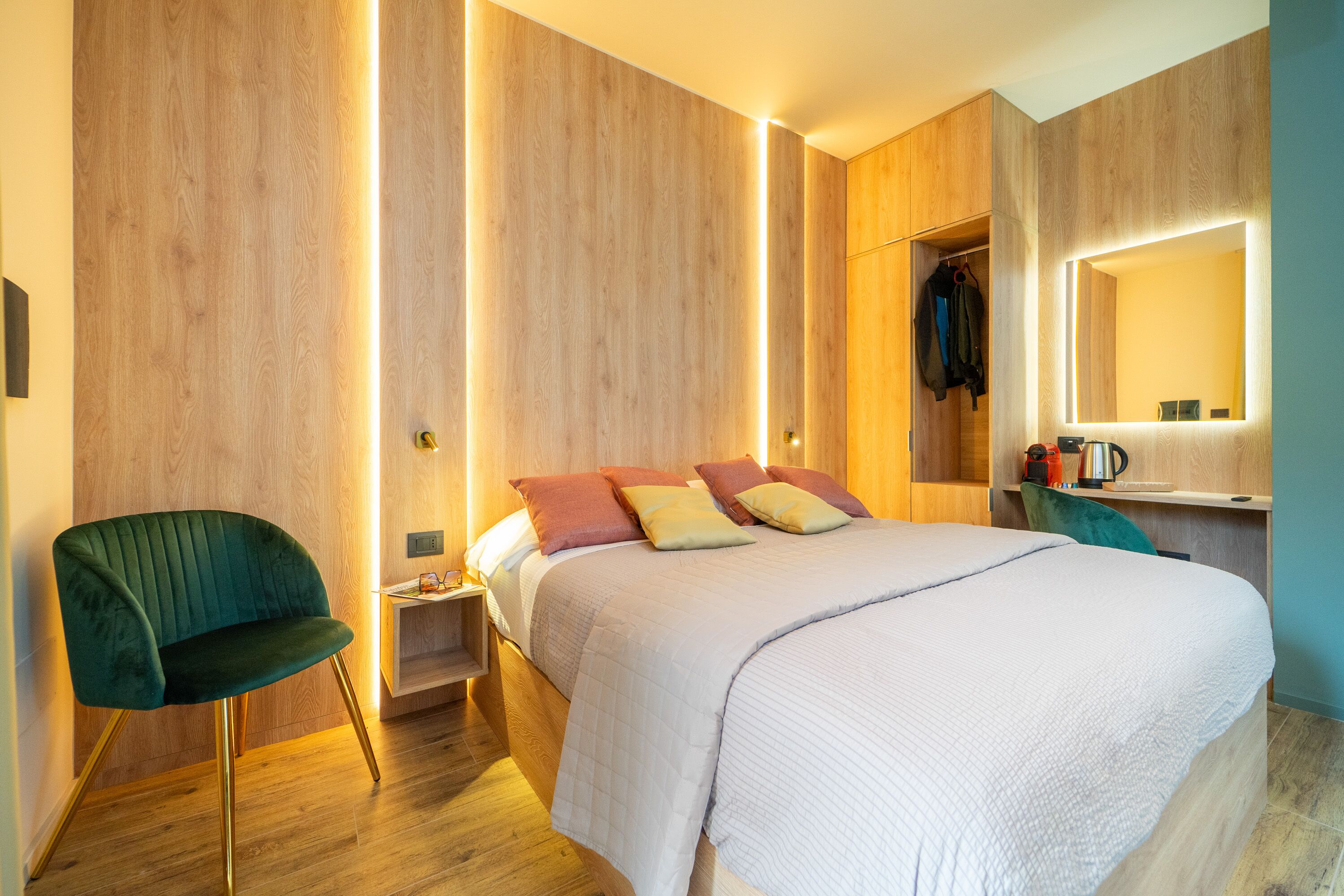 Quarto moderno com cama, uma cadeira verde, mesa de cabeceira e espelho.