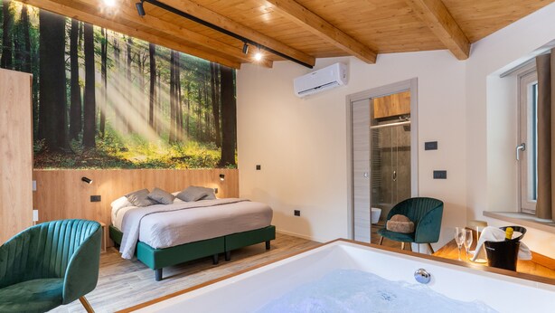 A modern bedroom with a large bed, a green chair, a bathtub, and a forest mural on the wall. - Villa dei Larici (Spezzano della Sila)
