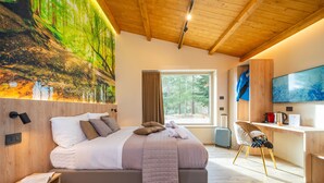 A modern bedroom with a large bed, a desk, a chair, a TV, and a painting of a forest. - Villa dei Larici (Spezzano della Sila)