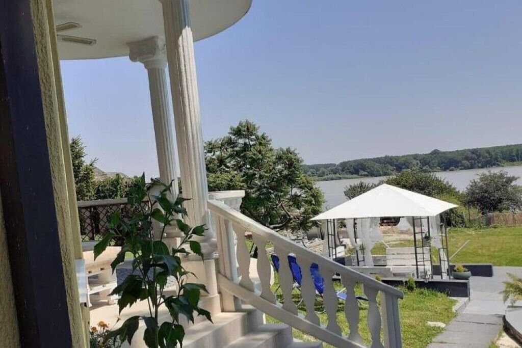 A covered outdoor area with a white railing, a gazebo, and a view of a lake.
