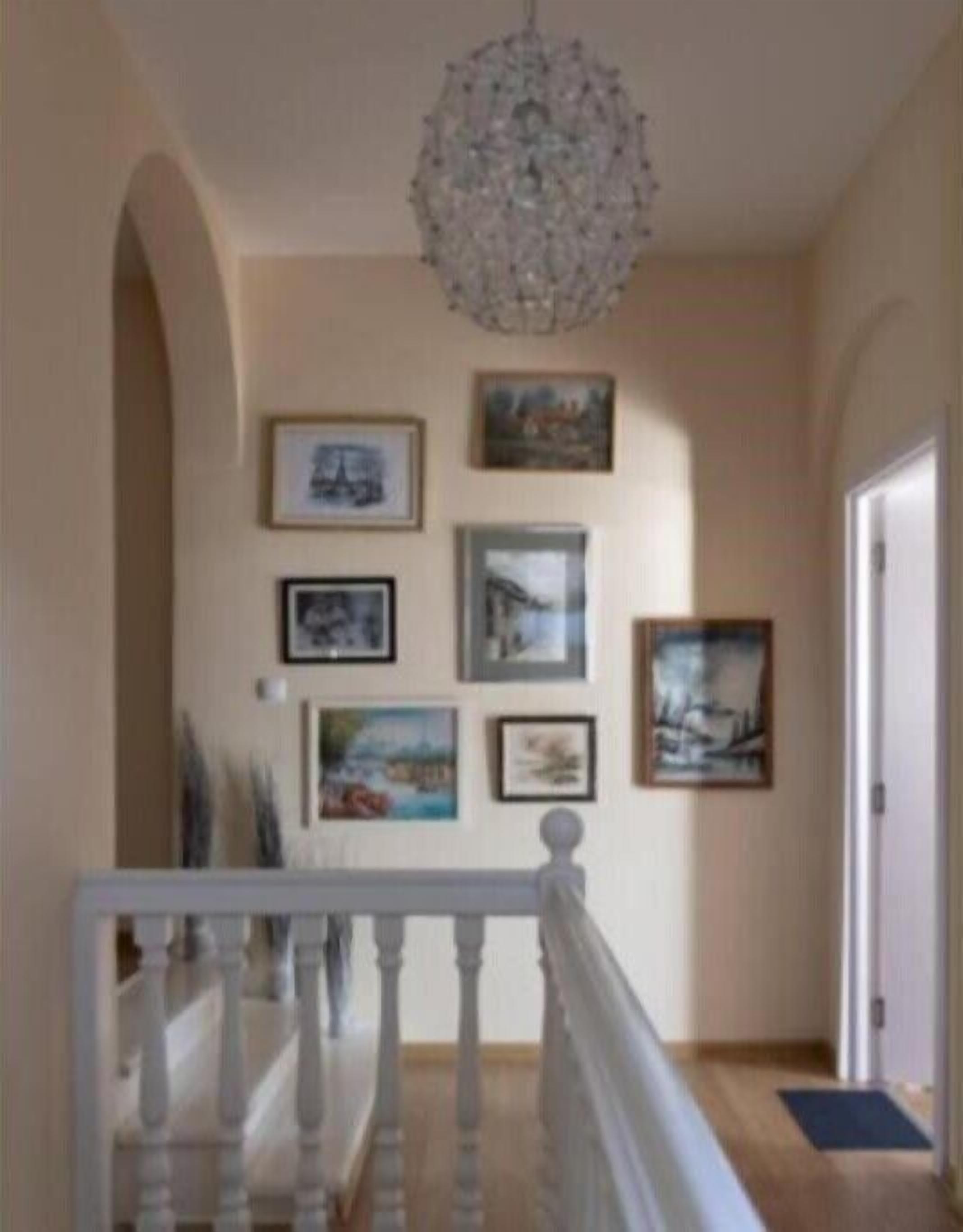 A hallway with a chandelier, framed artwork on the walls, and a wooden staircase.