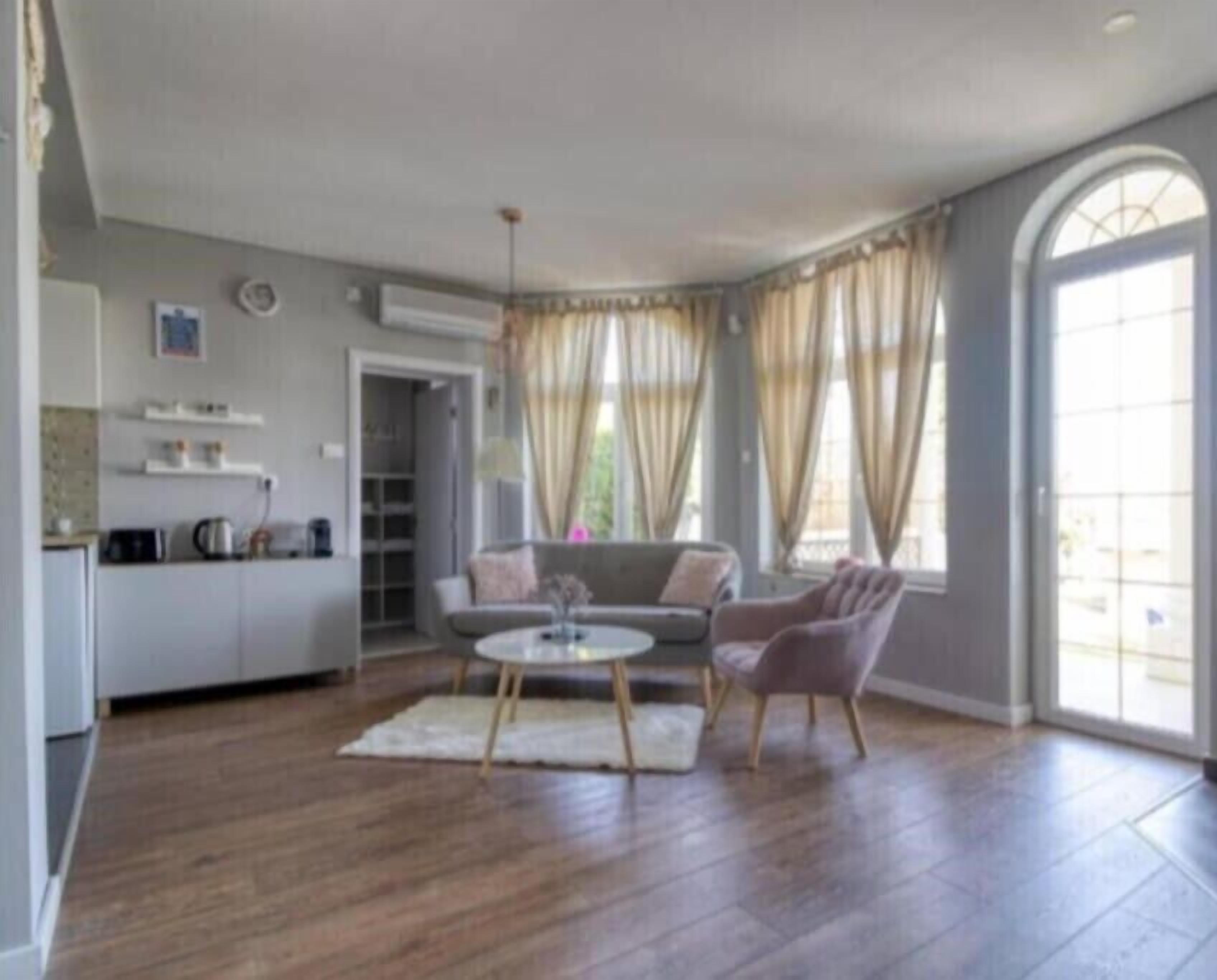 Amplia sala de estar con una mesa redonda, un sofá y un sillón. Hay una zona de cocina con encimera y armarios.