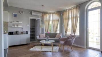 Amplia sala de estar con una mesa redonda, un sofá y un sillón. Hay una zona de cocina con encimera y armarios.