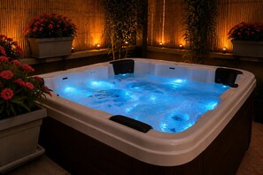 Uma banheira de hidromassagem iluminada em azul, rodeada por plantas em vasos e um fundo de bambu.