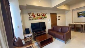 A living room with a TV, sofa, and coffee table. There is a painting on the wall and a door in the background.