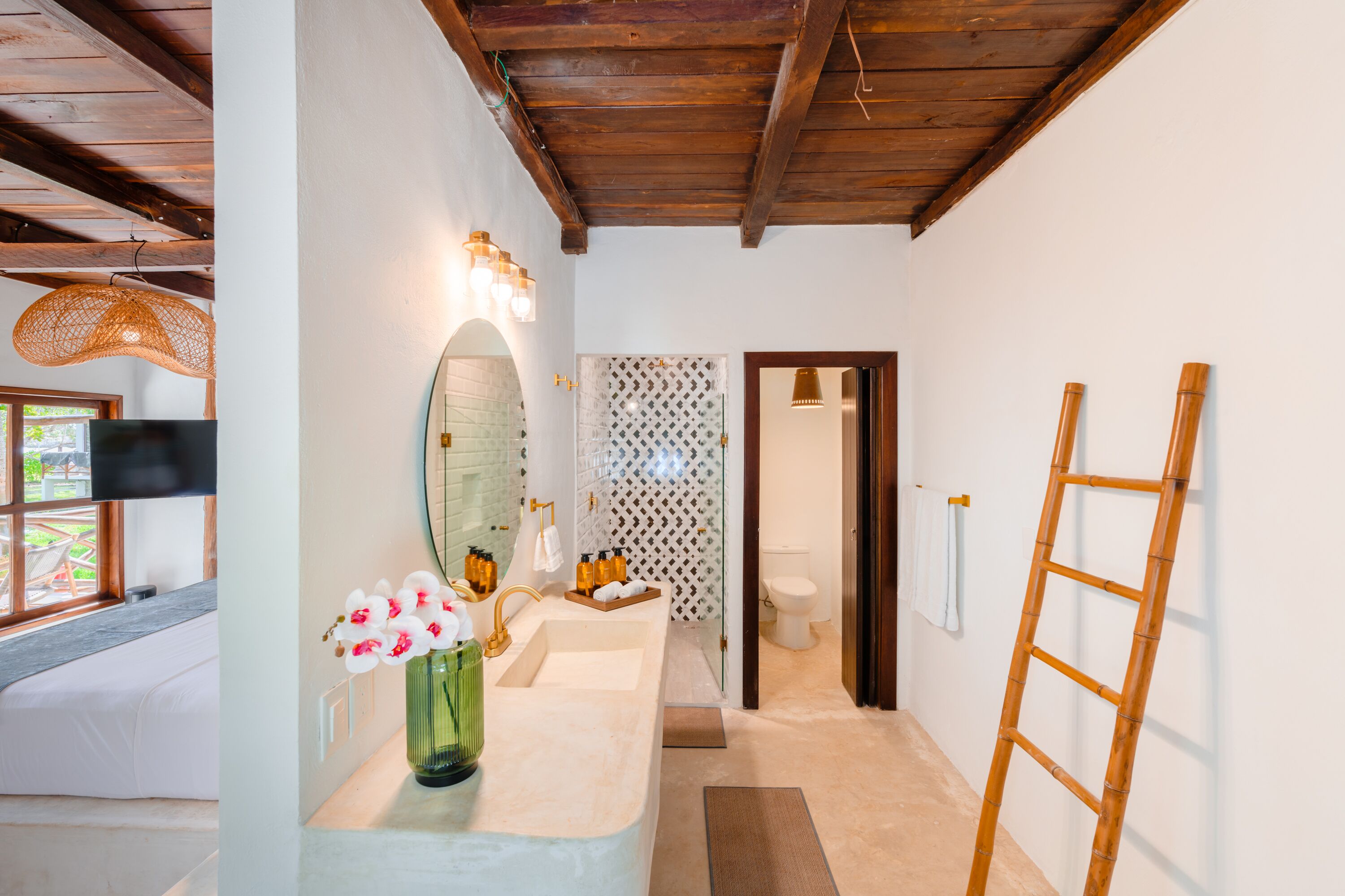 A bathroom with a wooden ceiling, a sink with a mirror, a toilet, and a shower area.