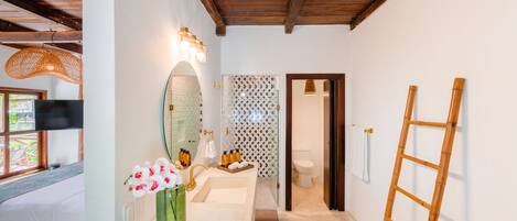 A bathroom with a wooden ceiling, a sink with a mirror, a toilet, and a shower area.