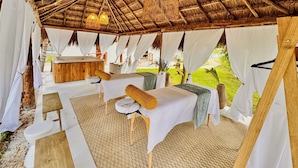 Un espace de spa extérieur doté d’un toit de chaume, de tables de massage, de tentures blanches et d’un banc en bois.