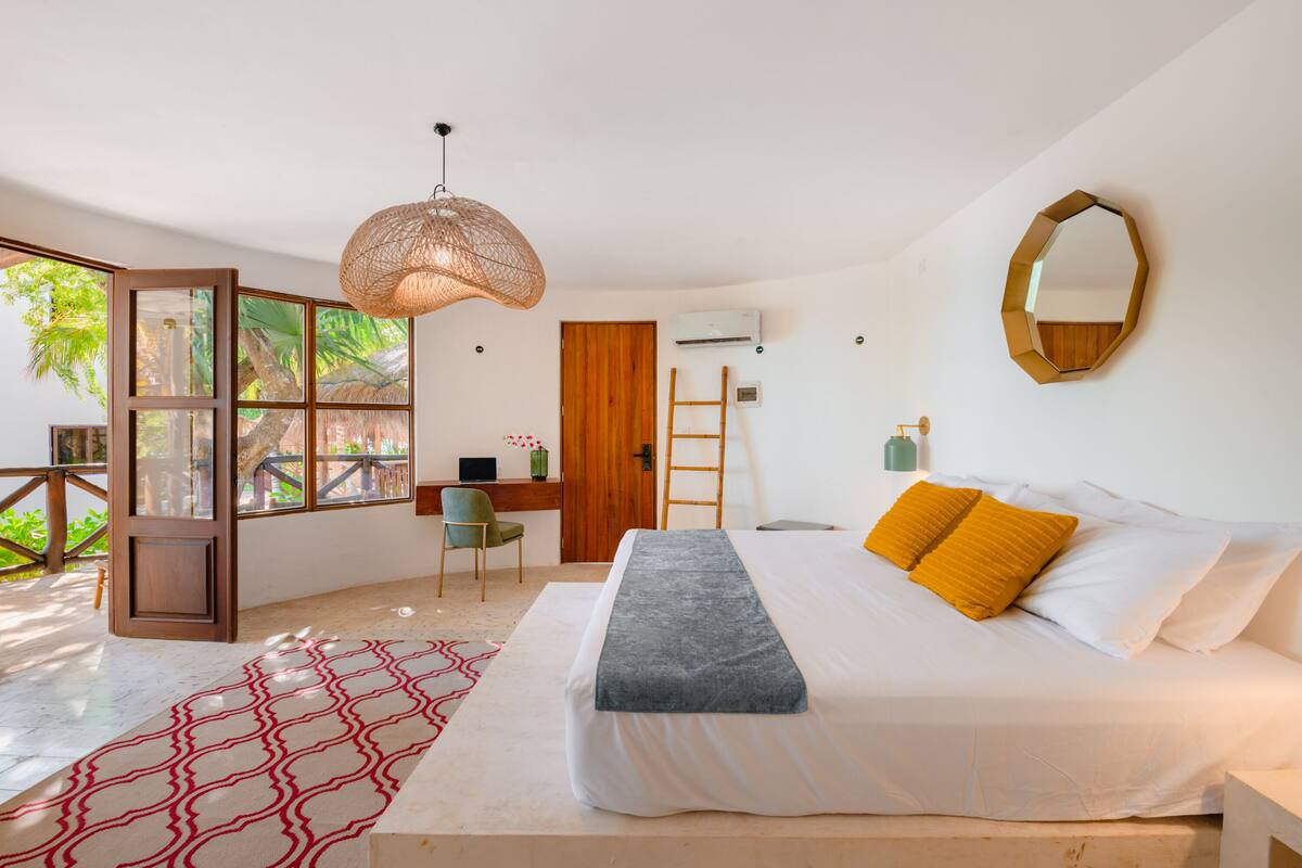 A bedroom with a bed, a desk, a chair, a ladder, and a large window.