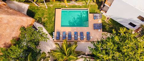Vista aérea de un área de piscina con piscina rectangular, rodeada de sillas de descanso y una pequeña terraza.