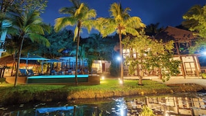 A pool area with lounge chairs and umbrellas, surrounded by palm trees and a building with a thatched roof. - Azulea Bacalar Hotel & Spa - Lagoon Front (Bacalar)