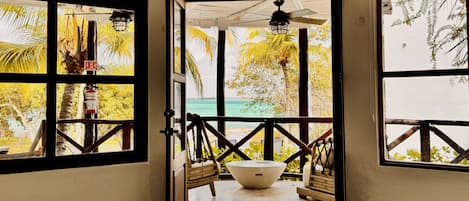 A view from a room with large windows to a beach, a ceiling fan, and a wooden table.