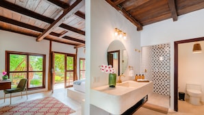 Une salle de bain moderne avec un grand lavabo, un miroir et une douche. Une chaise et un tapis se trouvent dans la pièce adjacente.