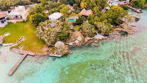 Vue aérienne d’une propriété située sur la côte, avec une piscine, plusieurs bâtiments et une jetée qui s’avance dans l’eau.