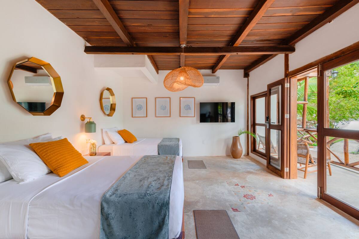 A bedroom with a large bed, two bedside tables, a TV, and a window with a view of greenery.