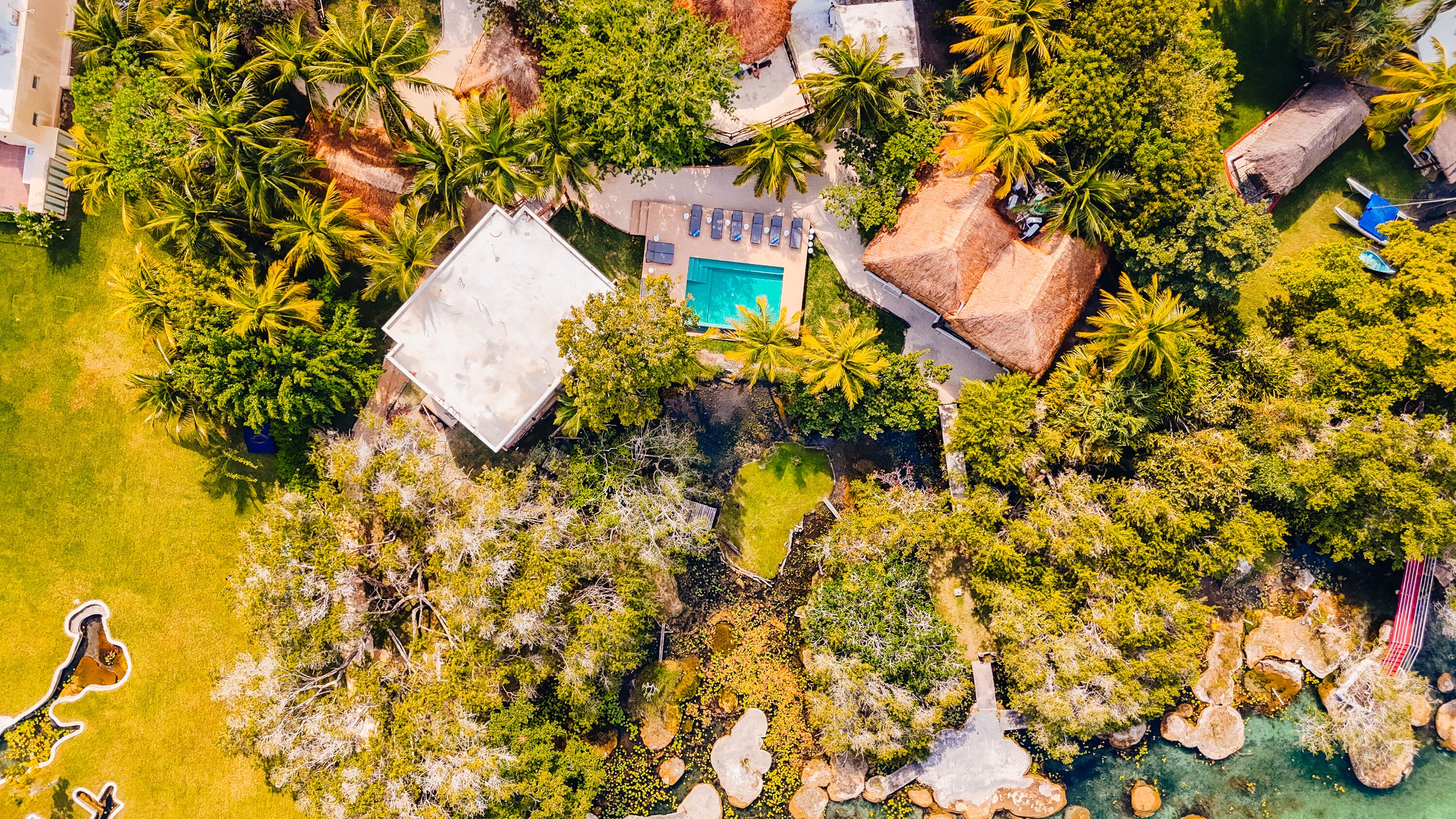Vue aérienne d’un complexe hôtelier doté d’une piscine, de palmiers et d’un bâtiment à toit de chaume.