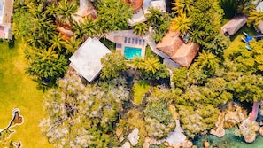 Vista aérea de un resort con piscina, palmeras y un edificio con techo de paja.