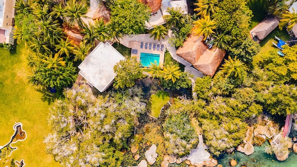 An aerial view of a resort with a swimming pool, palm trees, and a thatched-roof building. - Azulea Bacalar Hotel & Spa - Lagoon Front (Bacalar)
