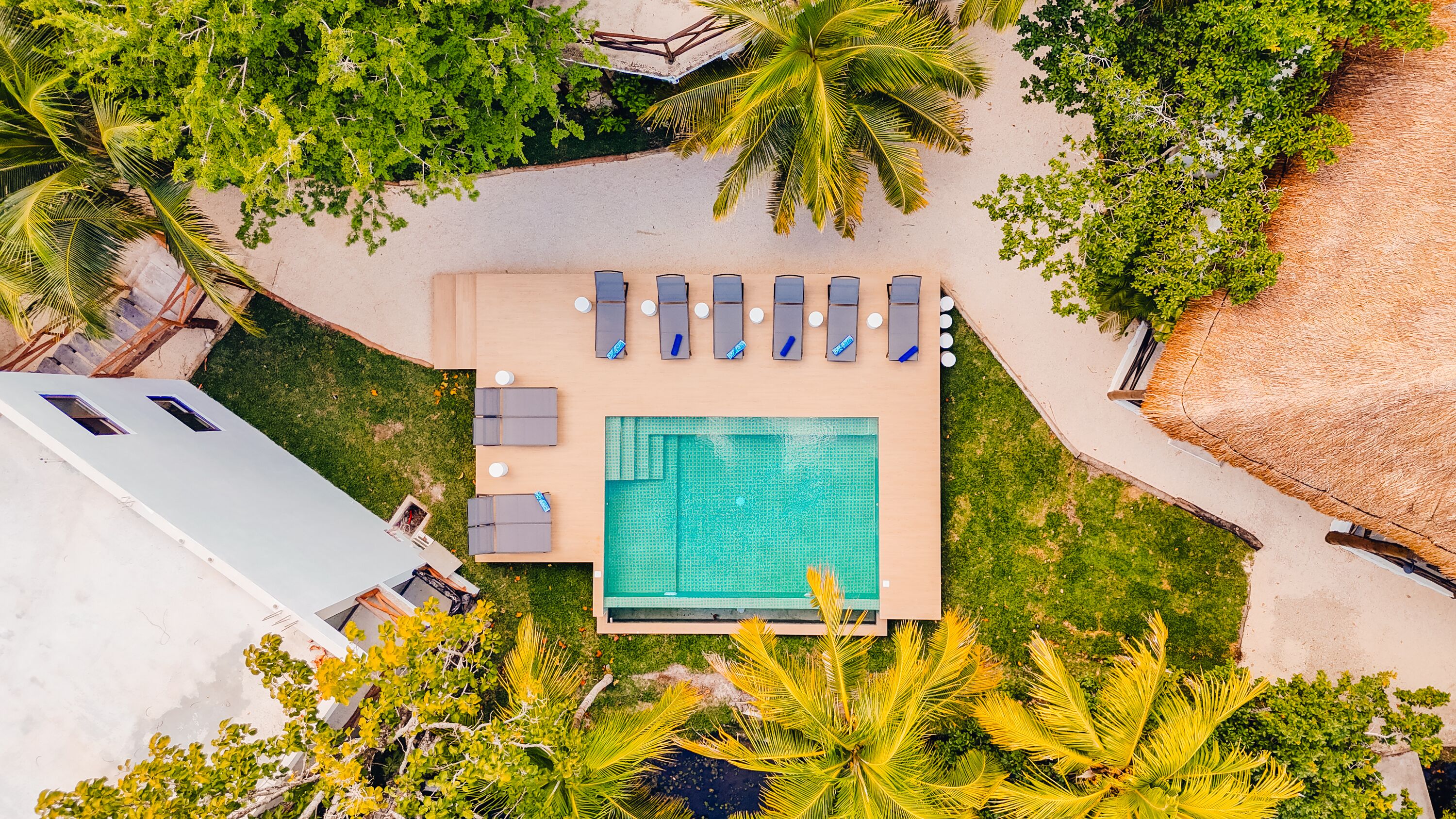 Vista aérea de uma área de piscina com uma piscina retangular, cadeiras de descanso e vegetação ao redor.
