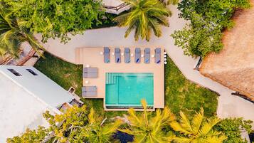 Vista aérea de uma área de piscina com uma piscina retangular, cadeiras de descanso e vegetação ao redor.