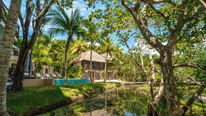 Un complexe hôtelier tropical doté d’une maison au toit de chaume, d’un petit étang parsemé de nénuphars et d’une végétation luxuriante.