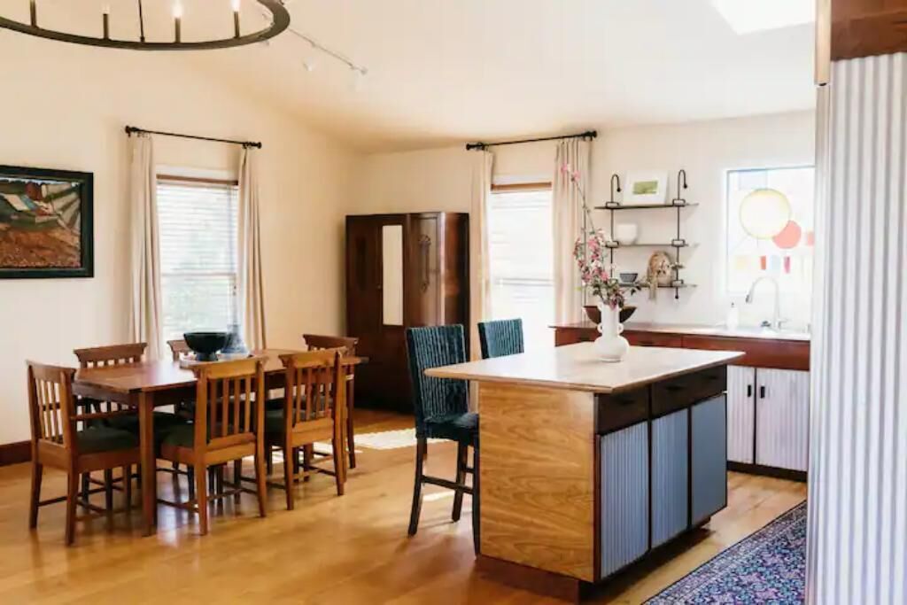 A modern kitchen with wooden cabinetry, a central island, and a dining area with wooden chairs.