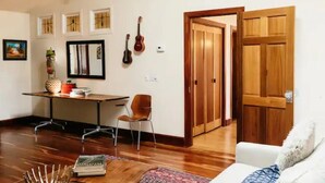 Ein Zimmer mit Holzboden, einem weißen Sofa, einem Schreibtisch mit Stuhl und einer Holztür.
