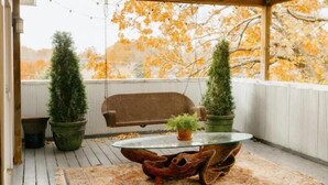 Eine überdachte Terrasse mit einem Glastisch, zwei Blumentöpfen, einem braunen Sofa und einem dekorativen Teppich.