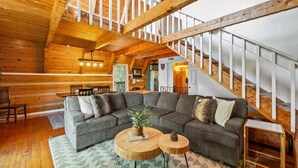 A spacious living room with a large sectional sofa, two round wooden coffee tables, and a staircase with white railings.