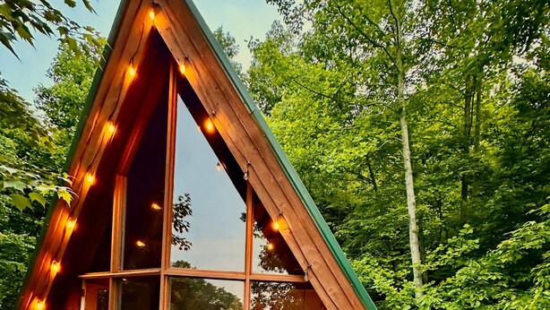 A wooden cabin with large windows and string lights, surrounded by trees.