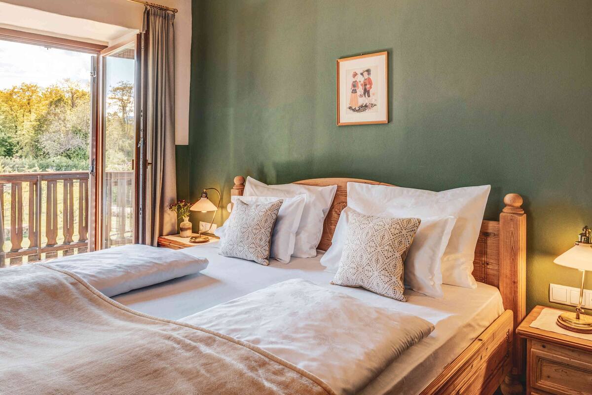 Une chambre d’hôtel avec un grand lit, une tête de lit en bois, une table de chevet avec une lampe et une vue sur l’extérieur grâce à une porte-fenêtre coulissante.
