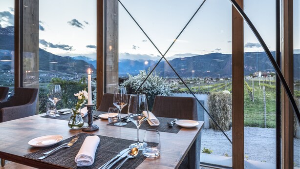 A dining table set for two with a candle, wine glasses, and cutlery, overlooking a mountainous landscape. - Ansitz Rungghof (Appiano Sulla Strada del Vino)
