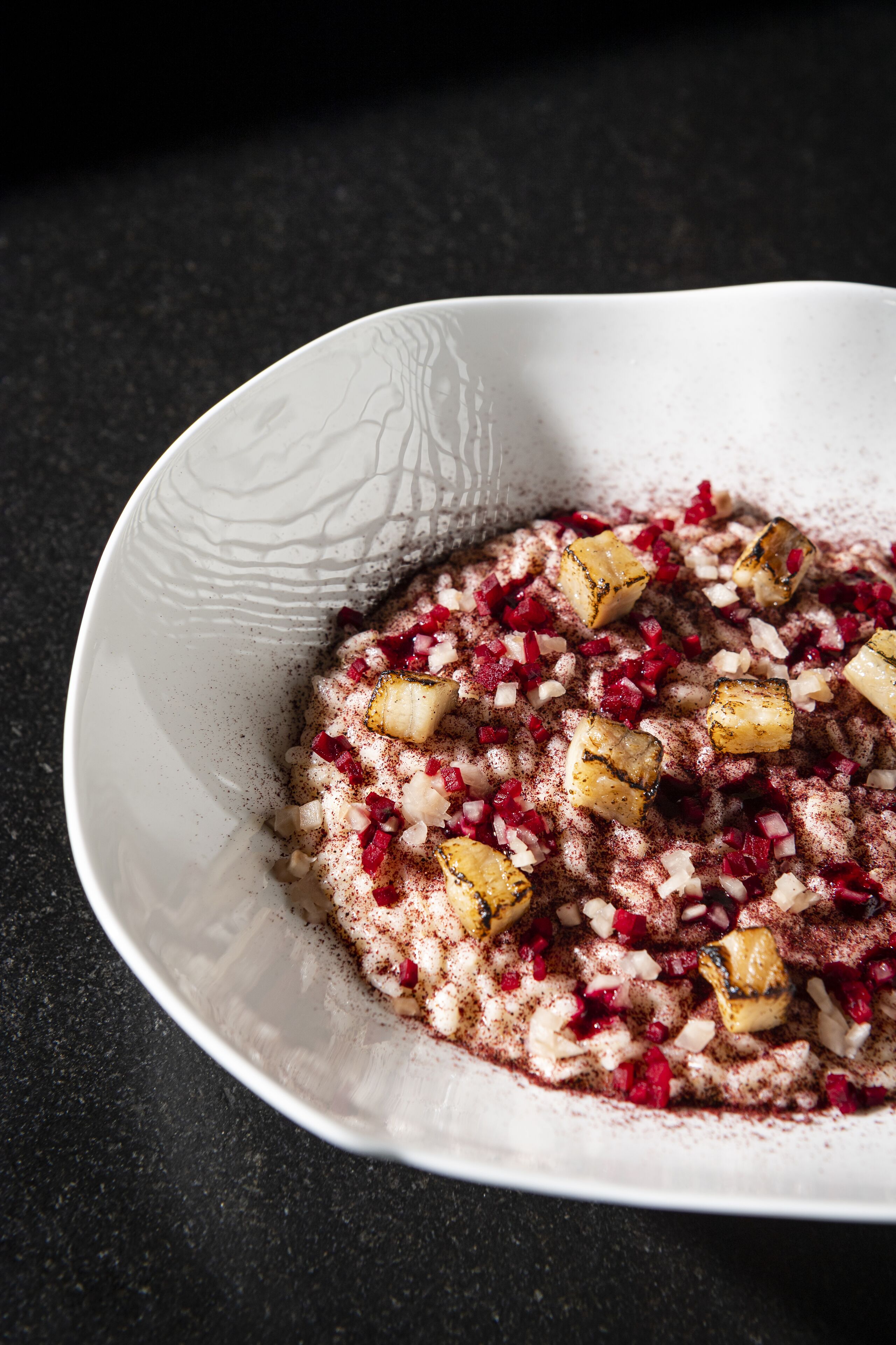 Un bol blanc orné d’un motif texturé, contenant des ingrédients rouges et blancs coupés en dés, probablement une salade de fruits ou un dessert.
