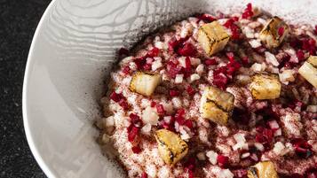Un bol blanc orné d’un motif texturé, contenant des ingrédients rouges et blancs coupés en dés, probablement une salade de fruits ou un dessert.