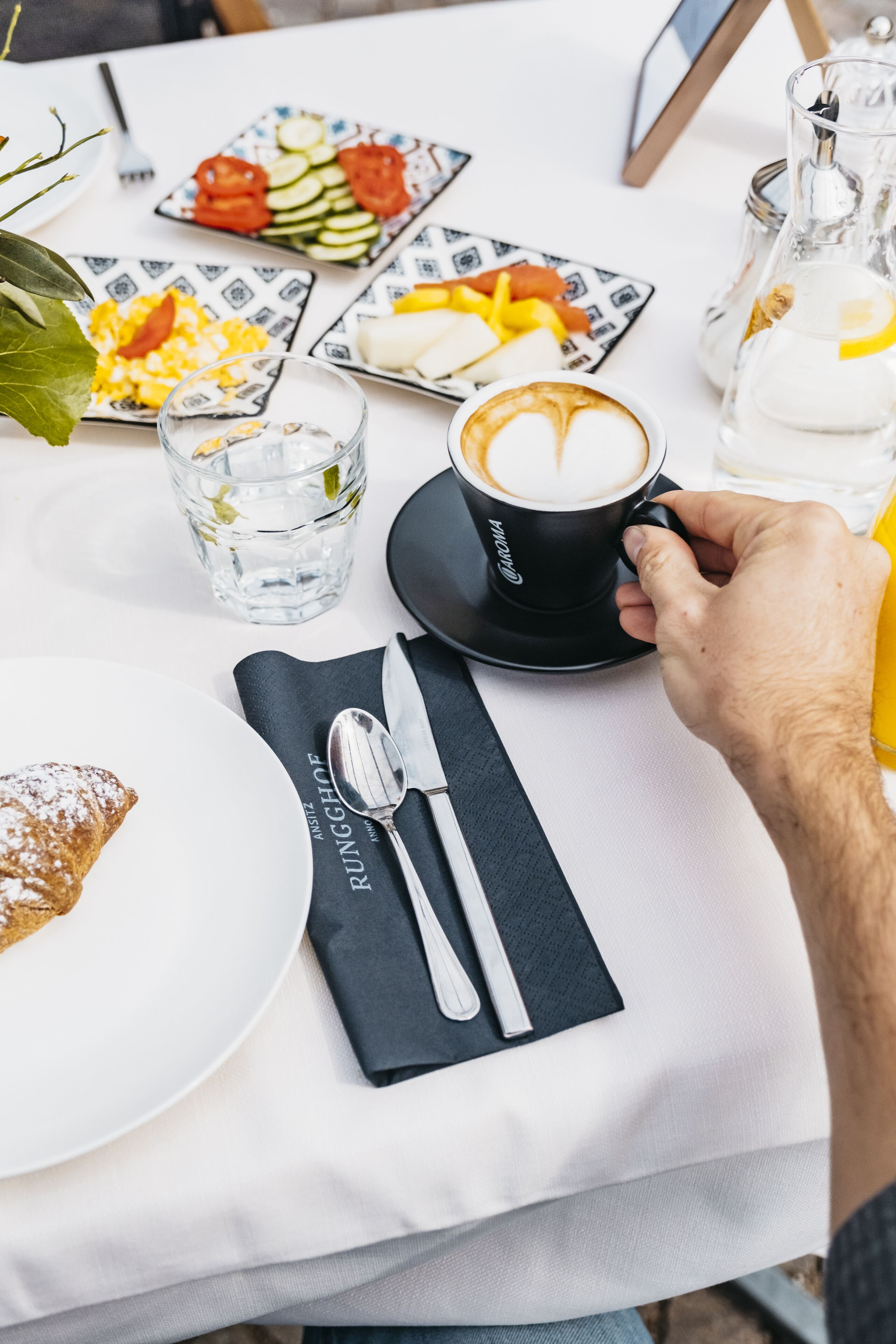A table set with a croissant, a plate of scrambled eggs, a glass of water, a cup of coffee, and a bottle of water.