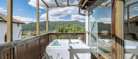 A balcony with a wooden railing, a white table, and a view of mountains.