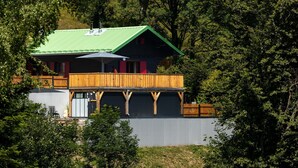 Una baita con tetto verde, veranda in legno e un ombrellone grande.