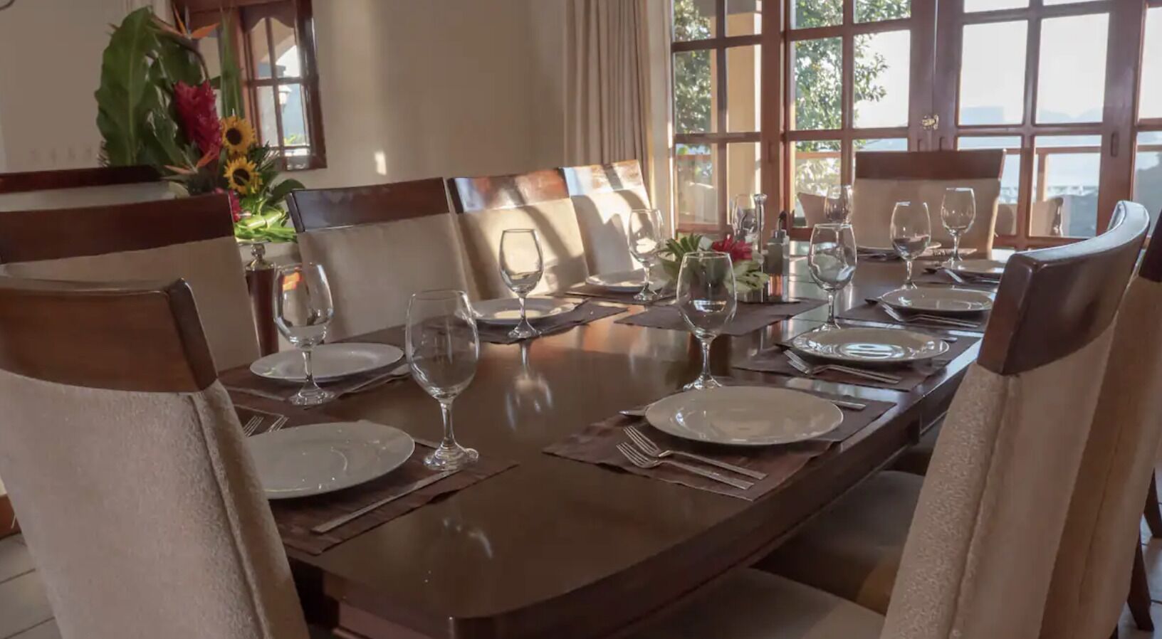 A dining table set for six with chairs, plates, cutlery, and wine glasses.
