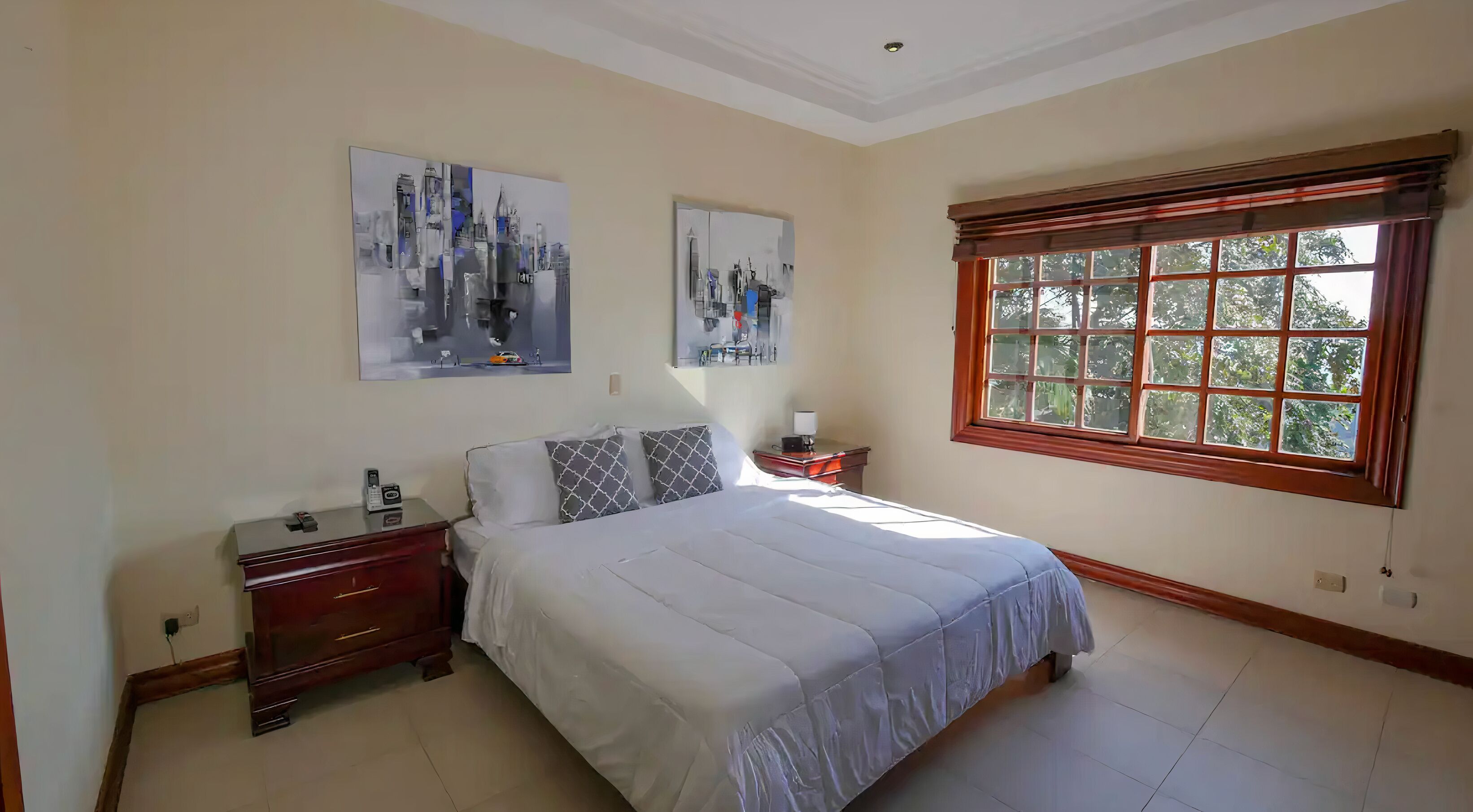 A bedroom with a bed, nightstands, a dresser, and two wall-mounted paintings.