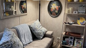A cozy living room with a beige sofa, patterned cushions, a floor lamp, a round painting, a bookshelf with various items, and a decorative mirror. - Escape to Bryson City, just a quick ride away from Great Smoky Mountains (Bryson City)