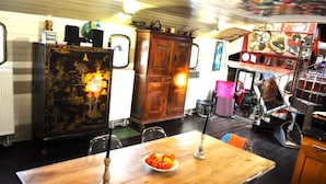 A dining area with a wooden table, chairs, and a bowl of fruit. There is a vintage cabinet with a decorative design and a globe on top. - Exceptionnel. Bateau Logement (Ailly-sur-Somme)