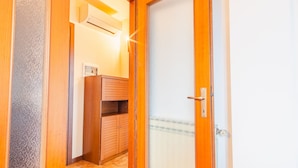 Un pasillo estrecho con un armario de madera, una puerta con manija y una unidad de aire acondicionado en la pared.
