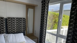 Une chambre à coucher avec un lit, une table de chevet, un miroir et une fenêtre avec des rideaux.