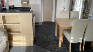 Une cuisine compacte équipée d’un four à micro-ondes, d’une cuisinière et de placards. Un coin repas avec une table et des chaises est également disponible.