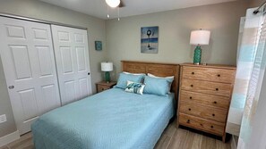 A bedroom with a bed, two nightstands, a wooden dresser, a painting, and a window with curtains.