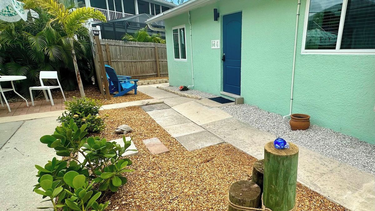 A small building with a blue door, a patio area with a table and chairs, and a garden with plants and gravel.