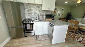 Una cocina compacta con armarios blancos, un refrigerador de acero inoxidable, un horno empotrado y un microondas.