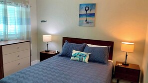 Habitación de hotel con cama, dos mesitas de noche, una lámpara, un cuadro y una ventana con cortinas.