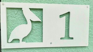 Un letrero blanco con la silueta de un ave y el número 1 sobre una pared verde con textura.